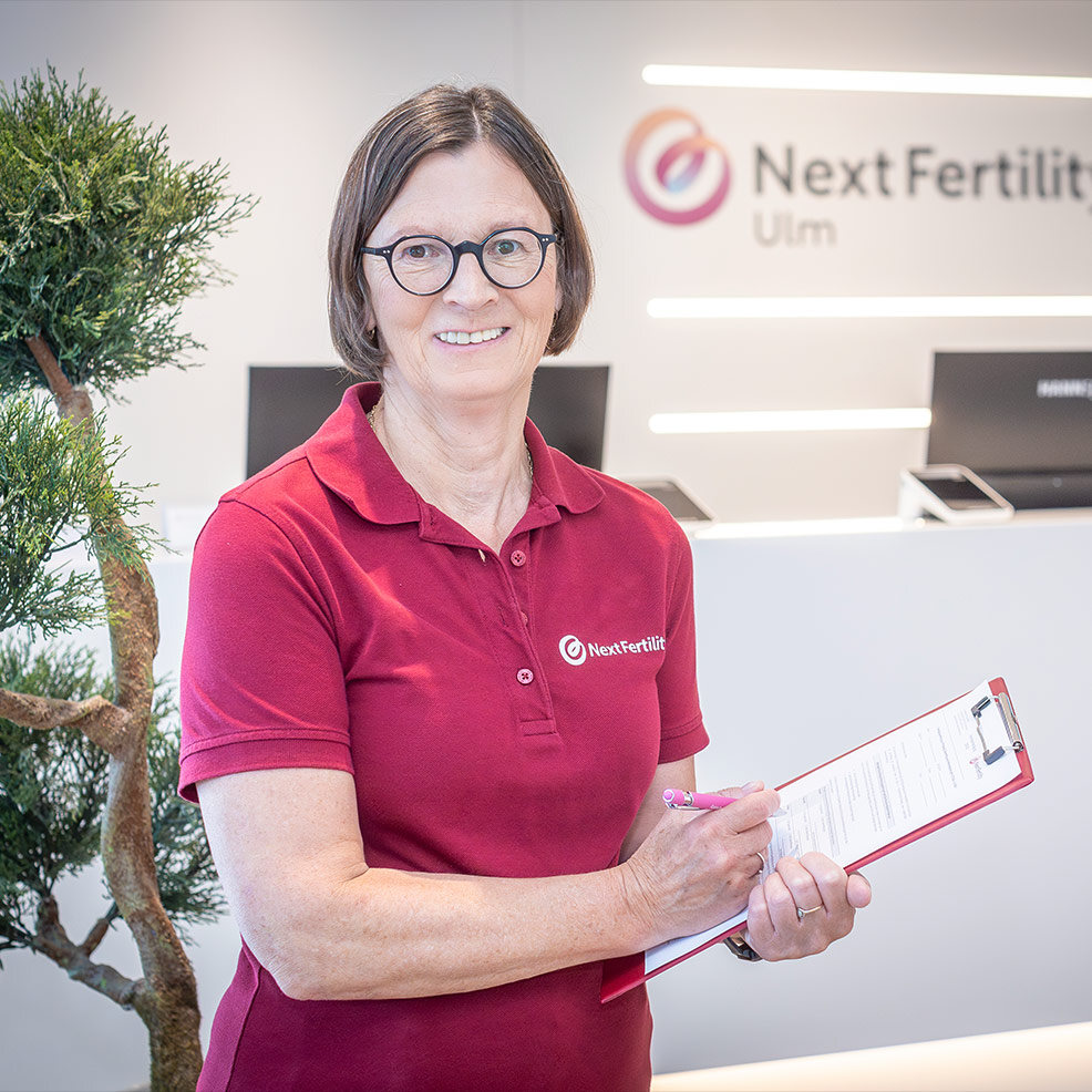 Eine Mitarbeiterin von Next Fertility Ulm schreibt etwas in ein Formular