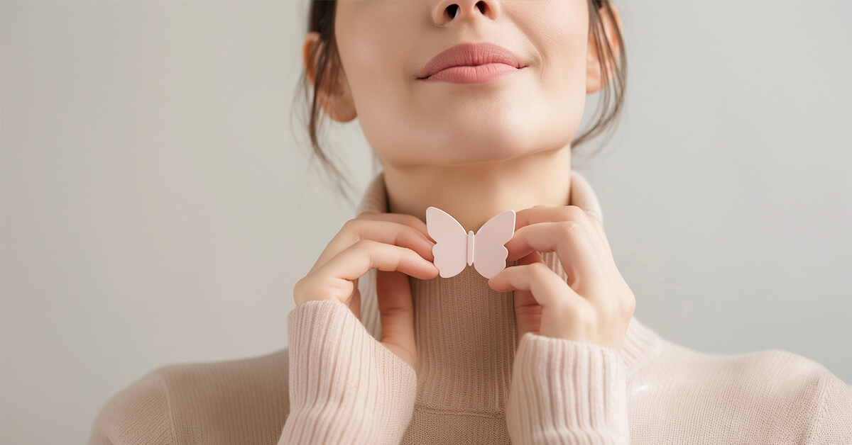 Zwei Hände einer Frau halten einen rosa Schmetterling in Höhe der Schilddrüse